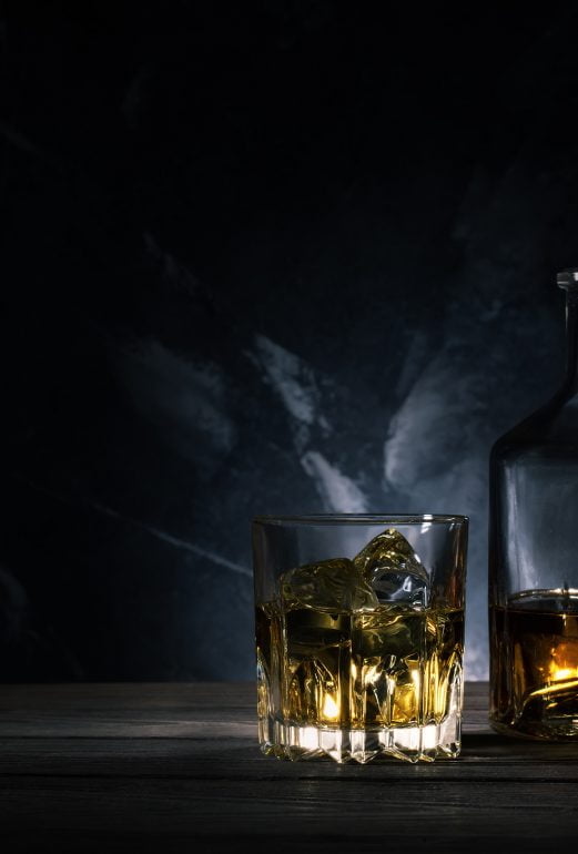 Glass of whiskey with ice, decanter and a wooden barrel
